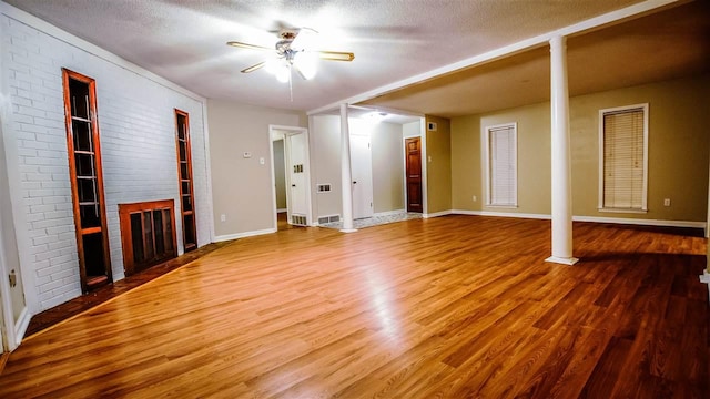 unfurnished living room featuring hardwood / wood-style floors, ceiling fan, brick wall, a brick fireplace, and a textured ceiling