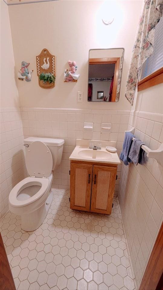 bathroom with toilet, vanity, tile walls, backsplash, and tile flooring