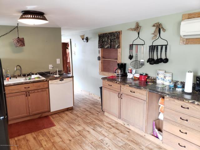 kitchen with dishwasher, a wall mounted AC, dark stone countertops, light wood-type flooring, and sink