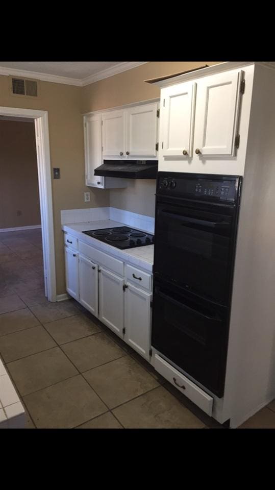 kitchen with dark tile flooring, ornamental molding, white cabinetry, and black appliances