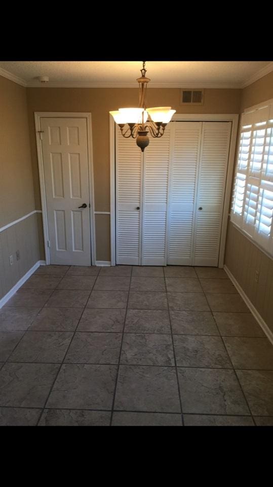 spare room featuring a chandelier, dark tile floors, and crown molding