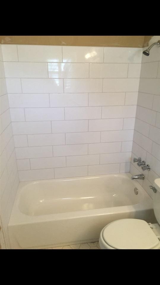 bathroom with tile flooring, toilet, and tiled shower / bath