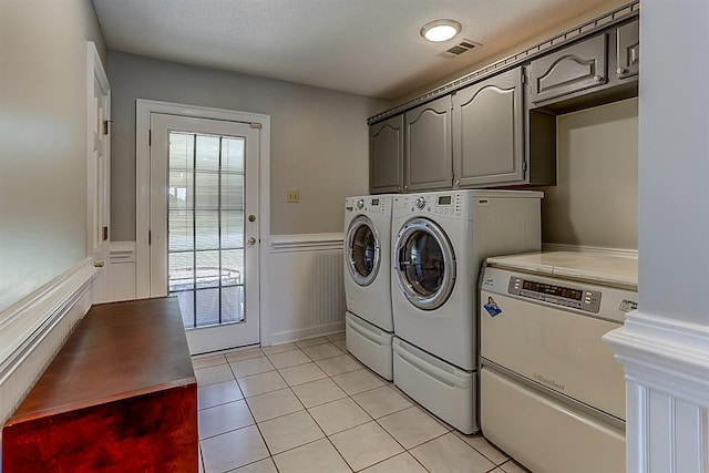 clothes washing area with washing machine and clothes dryer, cabinets, and light tile flooring