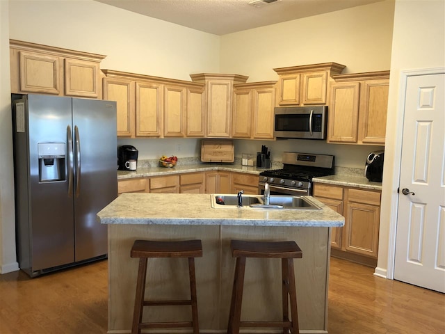 kitchen with a breakfast bar area, stainless steel appliances, sink, hardwood / wood-style flooring, and a center island with sink