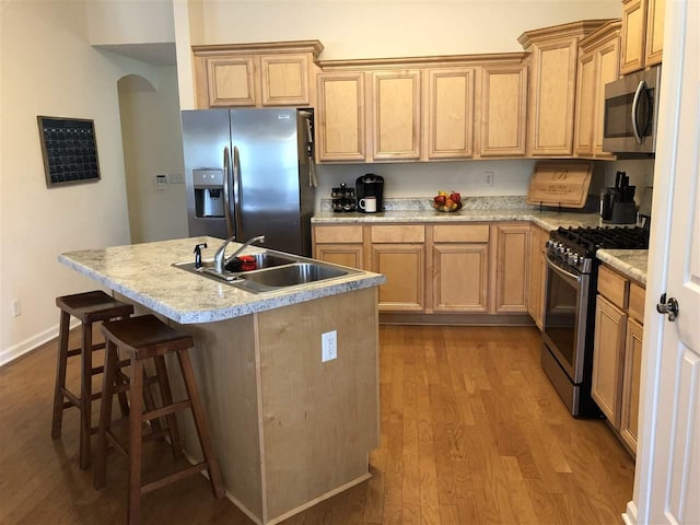 kitchen featuring a kitchen breakfast bar, appliances with stainless steel finishes, light hardwood / wood-style floors, sink, and light brown cabinetry