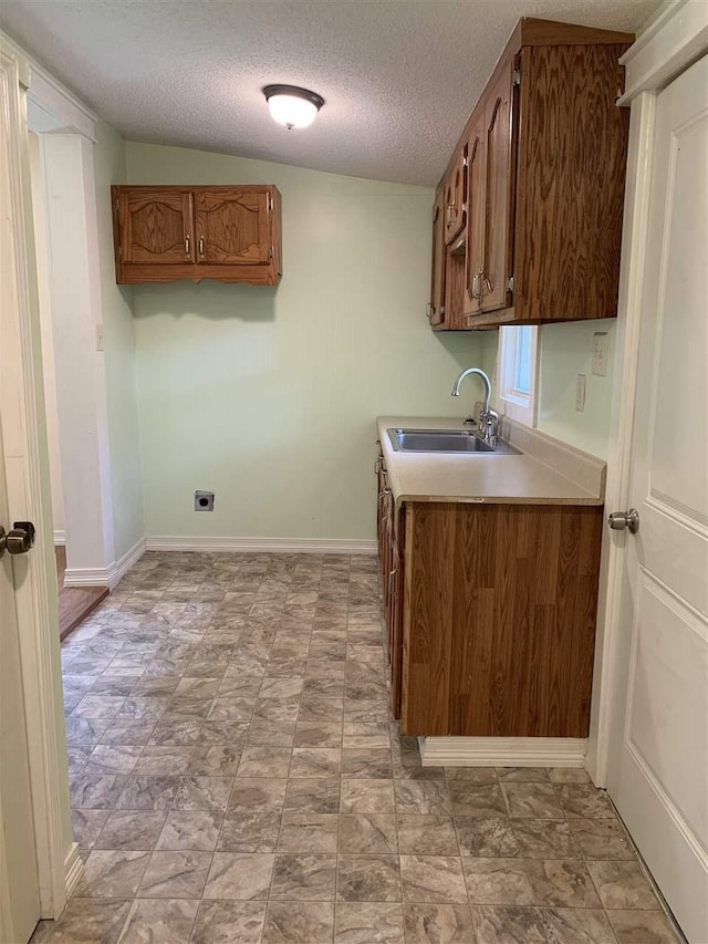 kitchen featuring a textured ceiling, sink, light tile floors, and vaulted ceiling