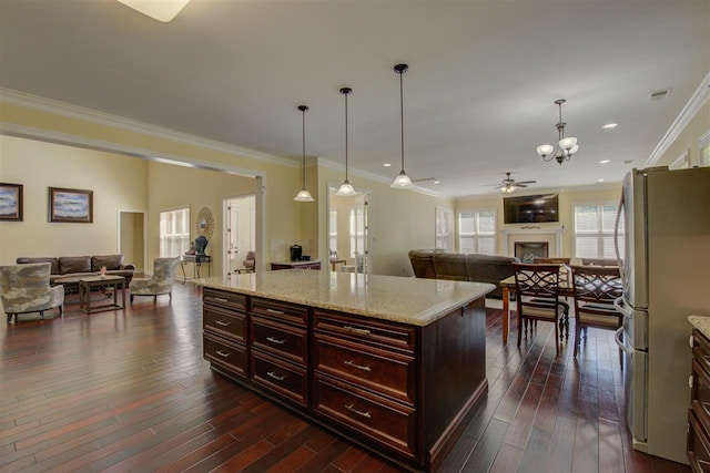 kitchen with hanging light fixtures, ornamental molding, stainless steel refrigerator, and dark wood-type flooring