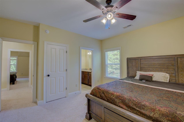 bedroom with ceiling fan, light colored carpet, and ensuite bath