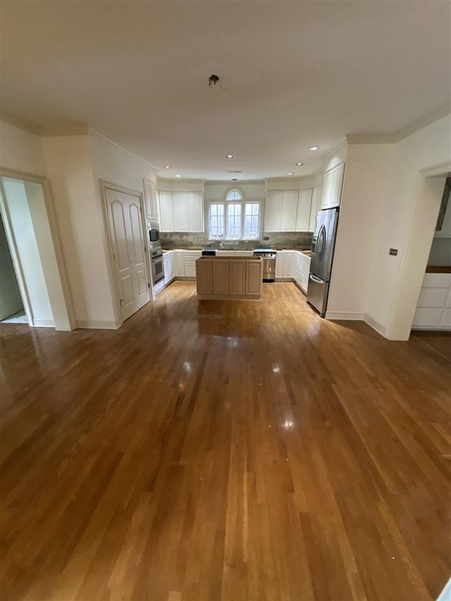 kitchen with appliances with stainless steel finishes, a center island, hardwood / wood-style floors, backsplash, and white cabinetry