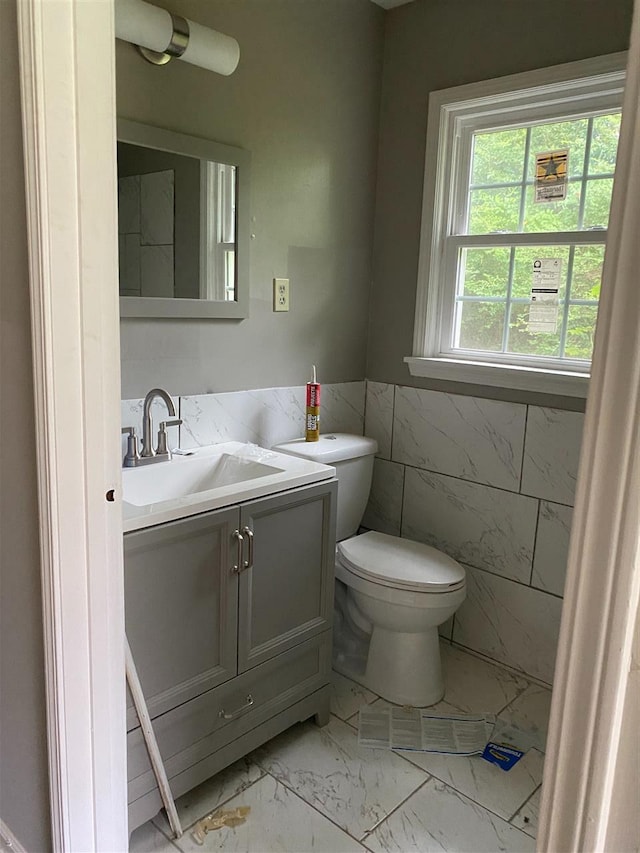 bathroom with tile flooring, tile walls, toilet, and vanity