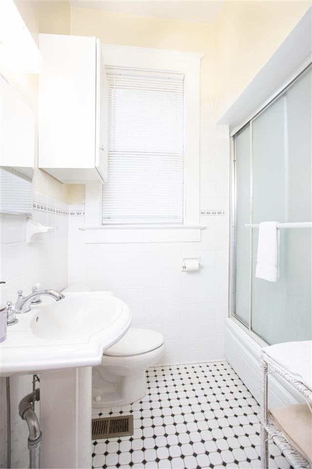 bathroom with tile flooring, a shower with shower door, toilet, and tile walls