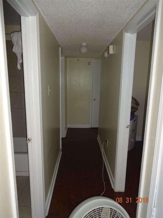 hallway featuring a textured ceiling and dark tile floors