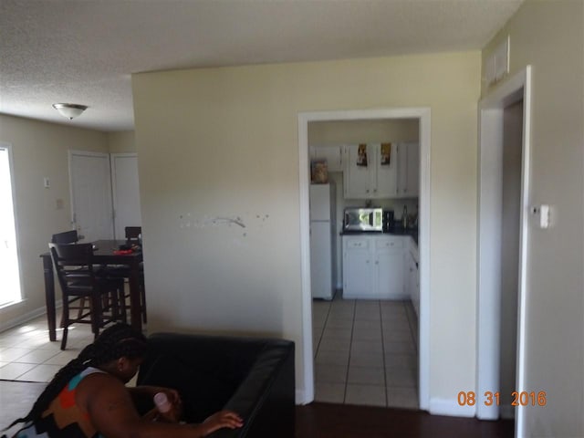 interior space with light tile floors, white cabinets, a textured ceiling, and white fridge