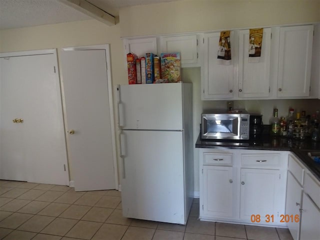 kitchen with white refrigerator, light tile flooring, and white cabinetry