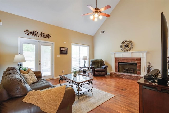 living room featuring high vaulted ceiling, a fireplace, ceiling fan, and light hardwood / wood-style flooring