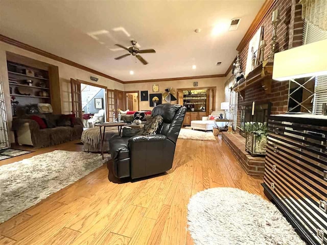 living room featuring ceiling fan, crown molding, a brick fireplace, and light hardwood / wood-style floors