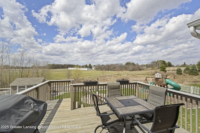 4246 Black Cherry Ln, Mason, MI 48854 - deck featuring a grill, outdoor dining area, a view of countryside, a playground, and an outdoor structure