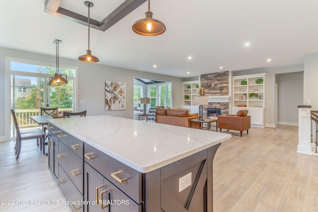 kitchen featuring decorative light fixtures, light stone counters, light hardwood / wood-style floors, a stone fireplace, and a center island