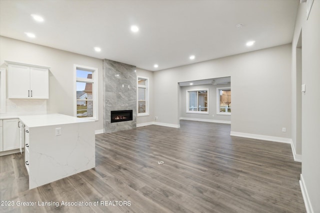 unfurnished living room featuring dark wood-type flooring, a wealth of natural light, and a tiled fireplace