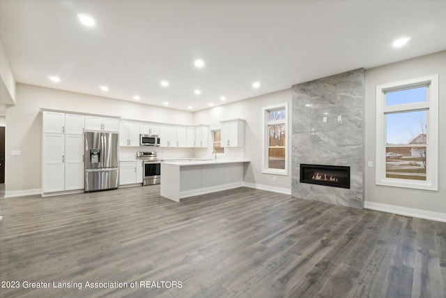 kitchen with a tile fireplace, appliances with stainless steel finishes, hardwood / wood-style flooring, white cabinets, and kitchen peninsula