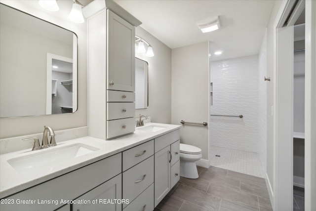 bathroom with toilet, double vanity, tile flooring, and tiled shower