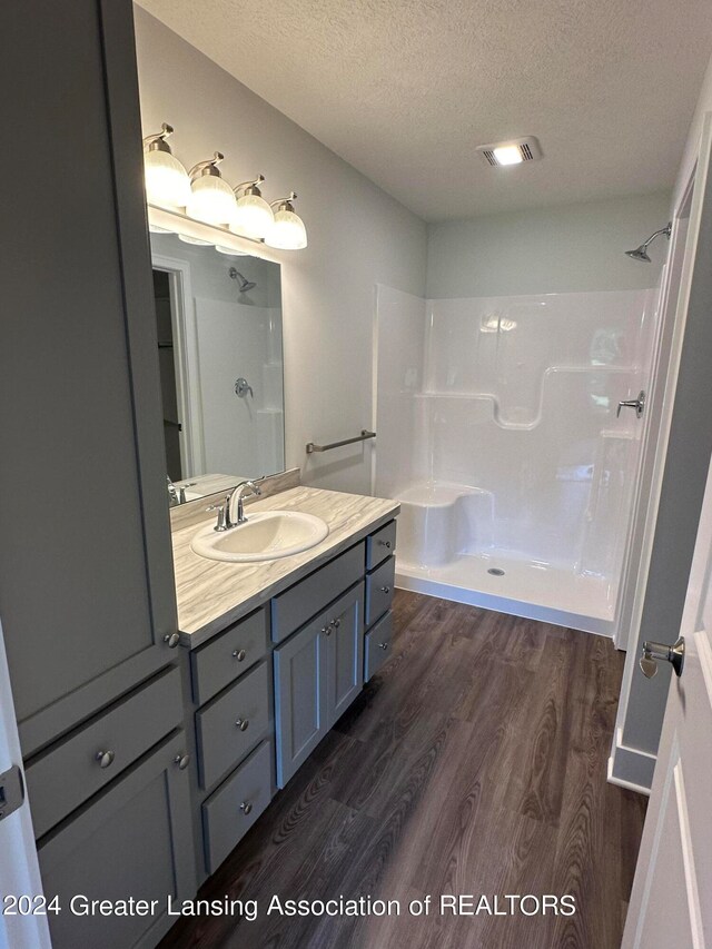 bathroom with walk in shower, hardwood / wood-style flooring, large vanity, and a textured ceiling