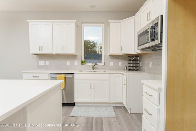 kitchen with tasteful backsplash, white cabinetry, sink, stainless steel appliances, and light wood-type flooring