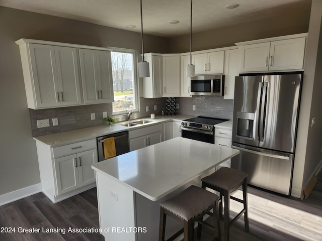 kitchen with sink, decorative light fixtures, appliances with stainless steel finishes, a kitchen island, and white cabinets