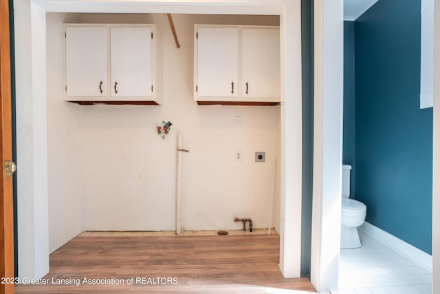 clothes washing area with cabinets, electric dryer hookup, and light hardwood / wood-style flooring