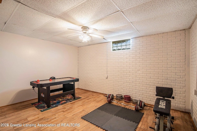 exercise area with brick wall, light wood-type flooring, ceiling fan, and a drop ceiling