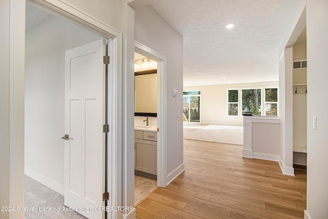 corridor with a textured ceiling, sink, and light wood-type flooring