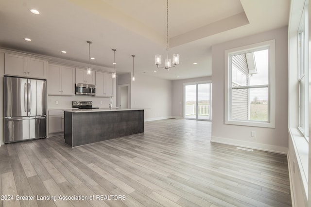 kitchen with appliances with stainless steel finishes, light hardwood / wood-style flooring, backsplash, hanging light fixtures, and an island with sink