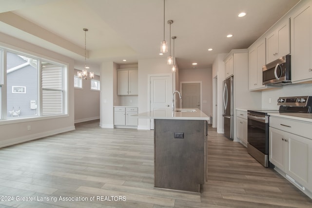 kitchen with hanging light fixtures, light hardwood / wood-style flooring, stainless steel appliances, and a center island with sink