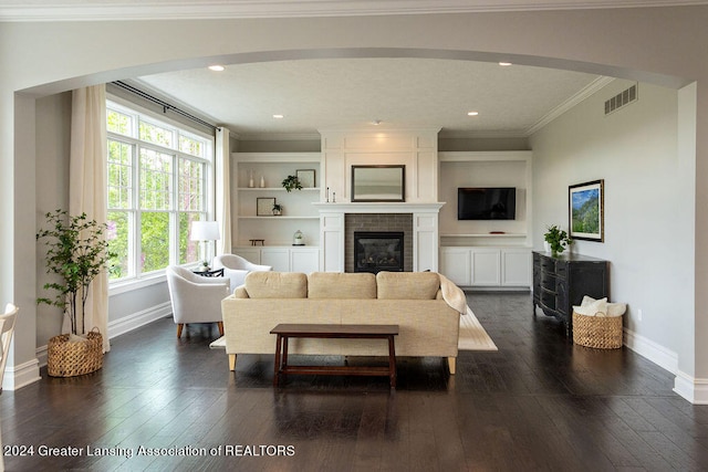 living room with built in shelves, crown molding, a large fireplace, and dark hardwood / wood-style floors