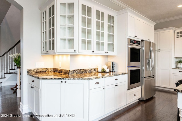 kitchen featuring white cabinets, crown molding, dark hardwood / wood-style floors, dark stone countertops, and stainless steel appliances