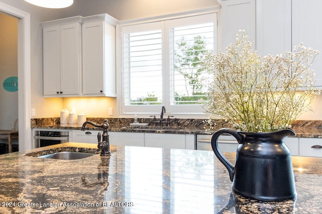 kitchen with stainless steel oven, dark stone countertops, white cabinetry, and sink