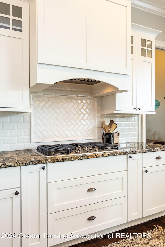 kitchen featuring tasteful backsplash, dark stone countertops, stainless steel gas stovetop, white cabinets, and ornamental molding