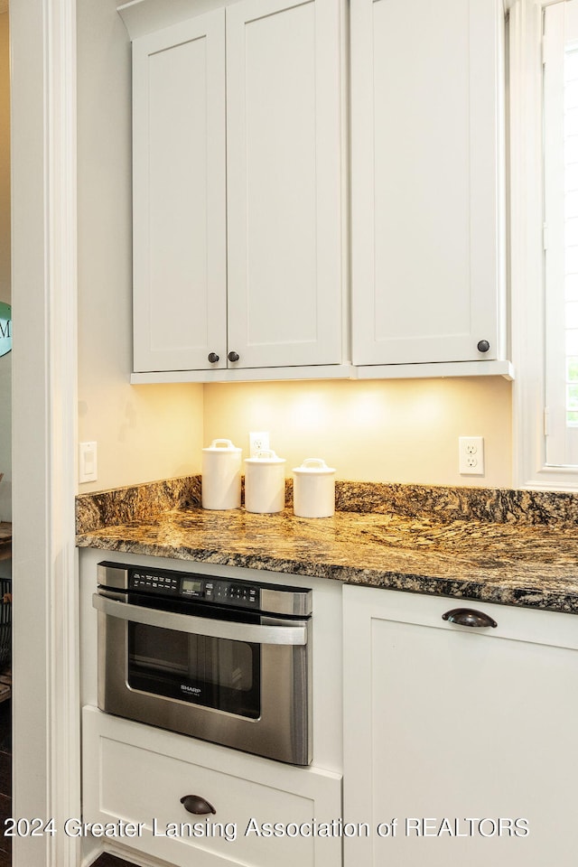 kitchen with dark stone countertops, white cabinets, and oven