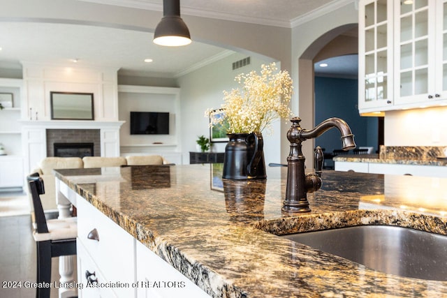 kitchen with sink, crown molding, pendant lighting, a fireplace, and white cabinets