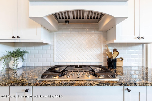 kitchen with stainless steel gas stovetop, exhaust hood, dark stone counters, decorative backsplash, and white cabinetry