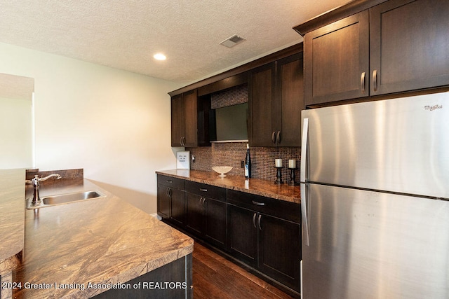 kitchen with dark hardwood / wood-style flooring, backsplash, dark brown cabinetry, sink, and stainless steel refrigerator