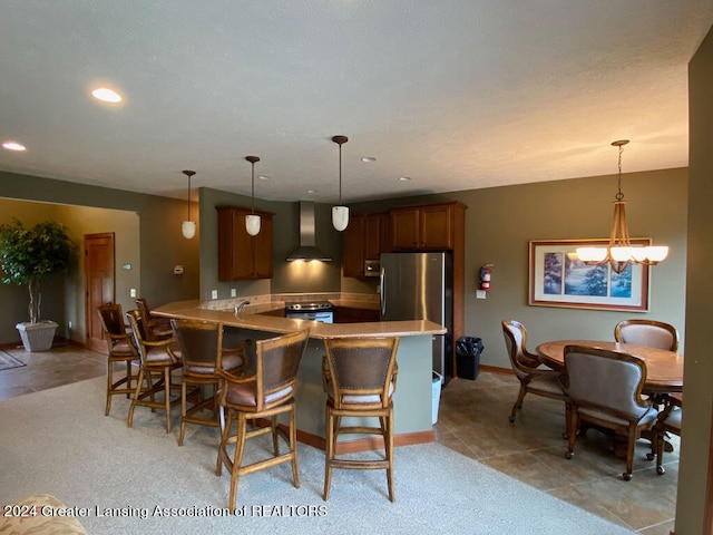 kitchen with kitchen peninsula, appliances with stainless steel finishes, a kitchen bar, wall chimney range hood, and hanging light fixtures