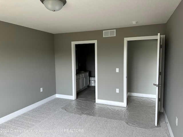 unfurnished bedroom featuring ensuite bath and dark colored carpet