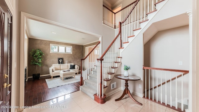 foyer with crown molding, light tile patterned floors, visible vents, a high ceiling, and baseboards