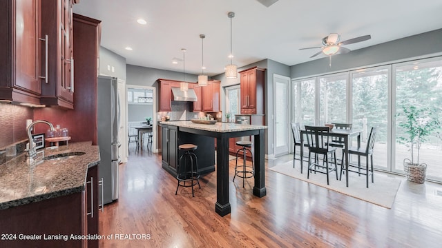 kitchen with a breakfast bar, a sink, wall chimney range hood, freestanding refrigerator, and decorative light fixtures