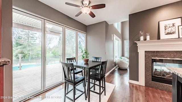 dining space featuring baseboards, dark wood finished floors, a ceiling fan, and a multi sided fireplace