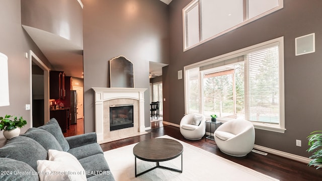 living area featuring a tile fireplace, a high ceiling, dark wood finished floors, and baseboards