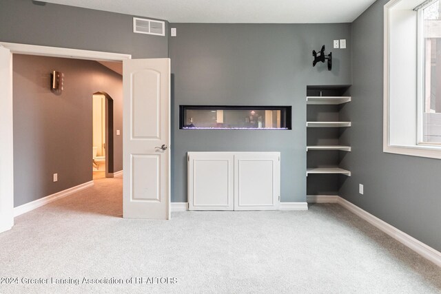 unfurnished living room featuring arched walkways, baseboards, visible vents, and light colored carpet