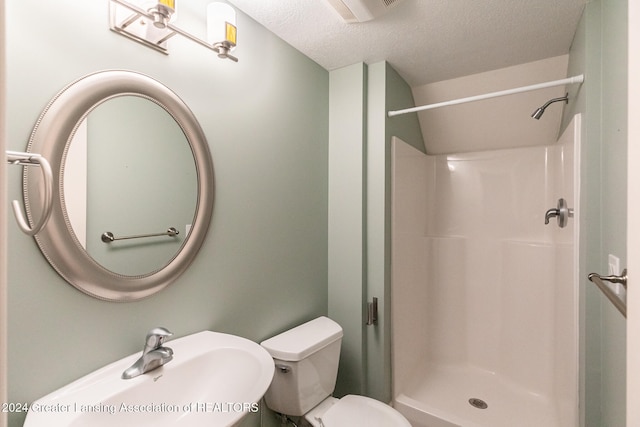 full bath featuring toilet, a sink, a textured ceiling, and a shower stall