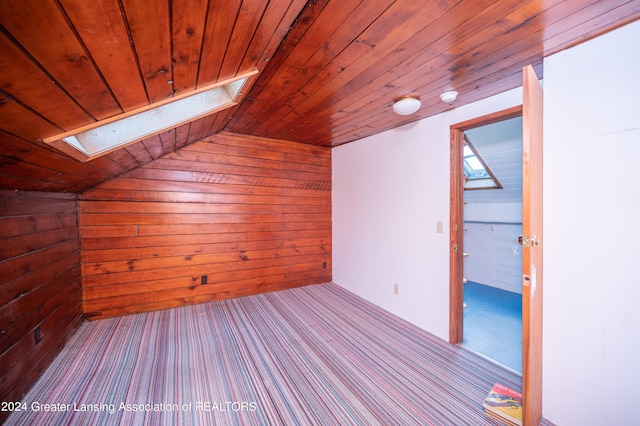 additional living space featuring wood ceiling, wood walls, vaulted ceiling with skylight, and light carpet